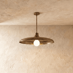 Clérachic pendant light in vintage brass, its wide disc shade and opal glass bulb hung from a plaster ceiling.