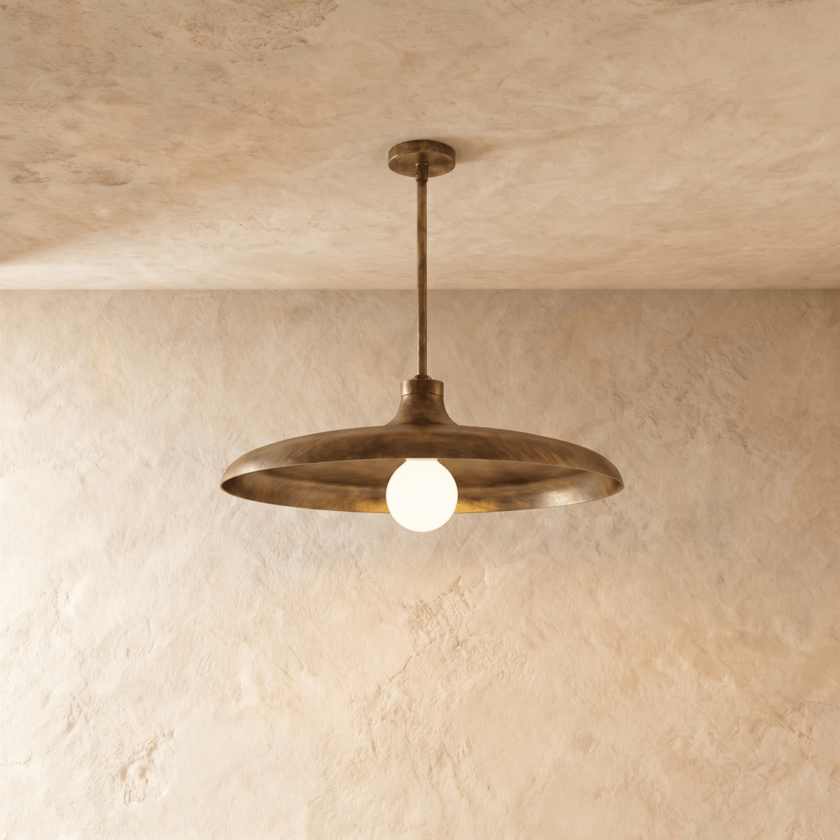 Clérachic pendant light in vintage brass, its wide disc shade and opal glass bulb hung from a plaster ceiling.