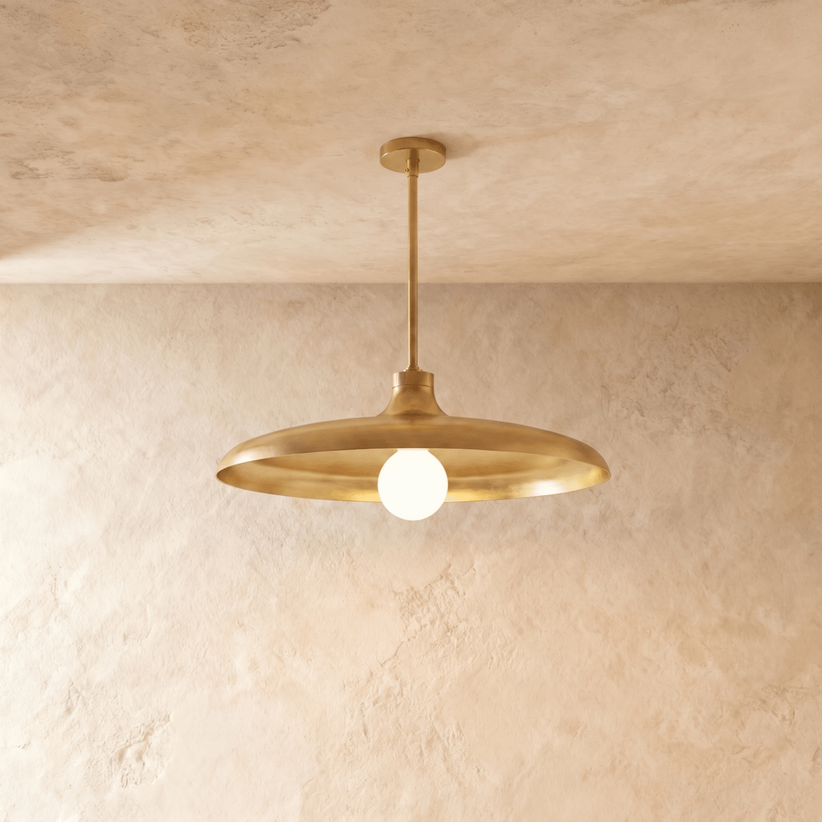 Clérachic pendant light in a brighter brass finish, its wide disc shade and opal glass bulb below a plaster ceiling.