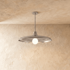 Clérachic pendant light in a bright chrome finish, its wide disc shade and opal glass bulb below a plaster ceiling.