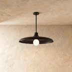 Clérachic pendant light in matte black, its wide disc shade and opal glass bulb hung from a plaster ceiling.
