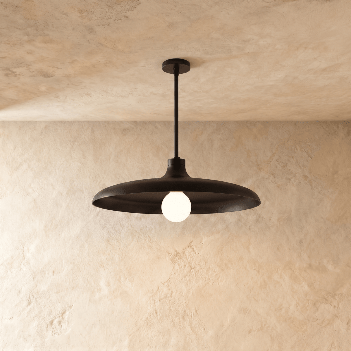 Clérachic pendant light in matte black, its wide disc shade and opal glass bulb hung from a plaster ceiling.