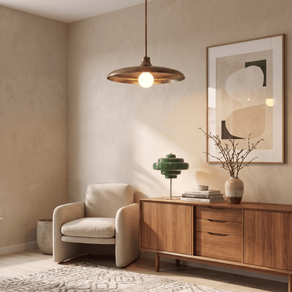 Clérachic brass pendant light glowing above a beige armchair and walnut credenza styled with a green table lamp.
