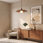 Clérachic brass pendant light glowing above a beige armchair and walnut credenza styled with a green table lamp.
