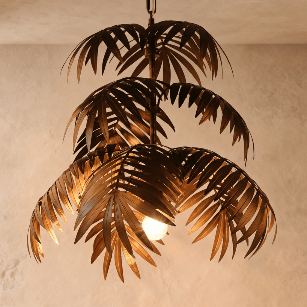 Clérachic tiered palm-leaf chandelier in aged bronze iron, lit by a single warm bulb, hung on a limewash wall.
