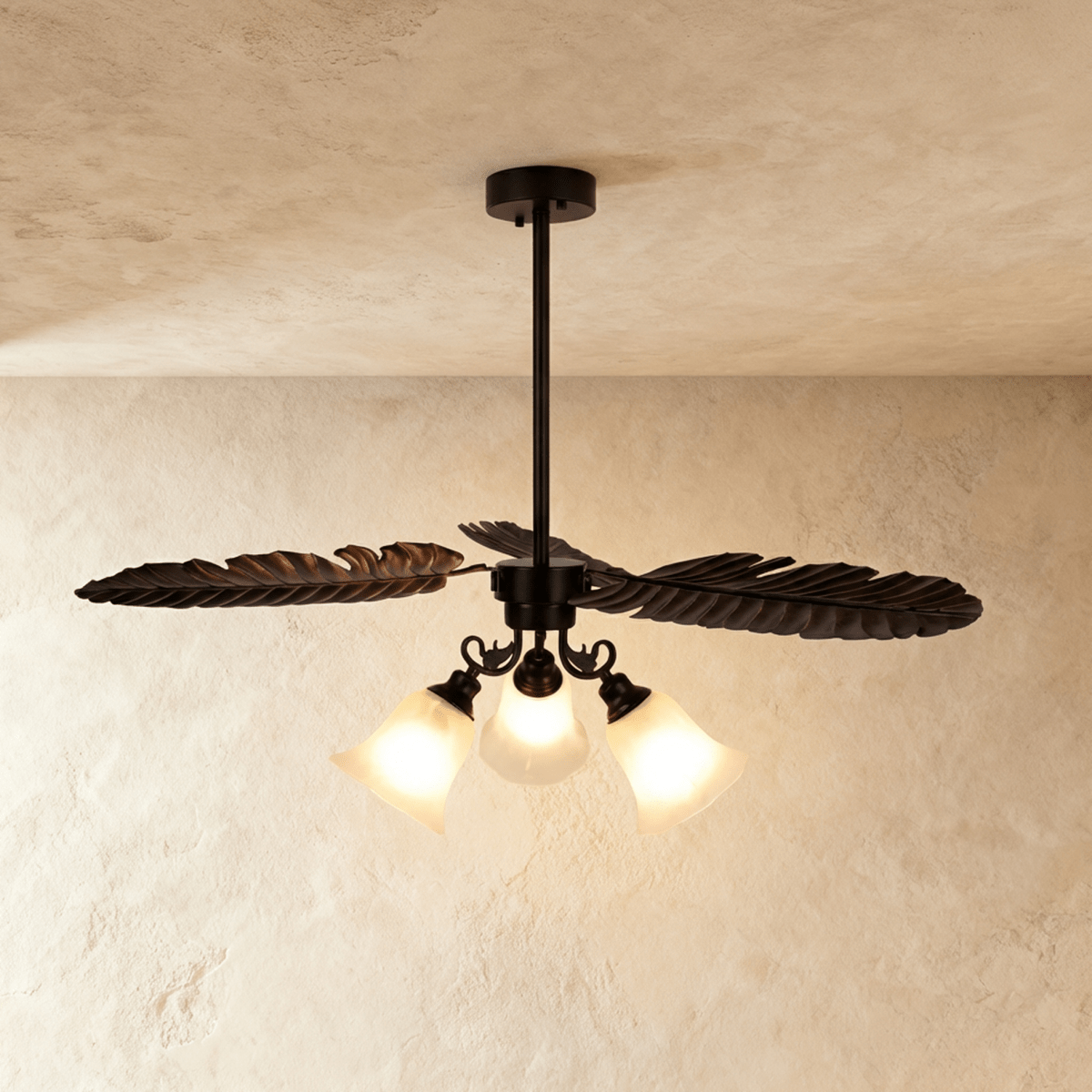 Clérachic dark bronze ceiling light with three long iron palm leaves above three frosted glass bell shades, glowing warm.
