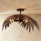 Clérachic ceiling-mounted palm-leaf light in dark bronze iron, fronds sweeping down over warm bulbs on a short drop.