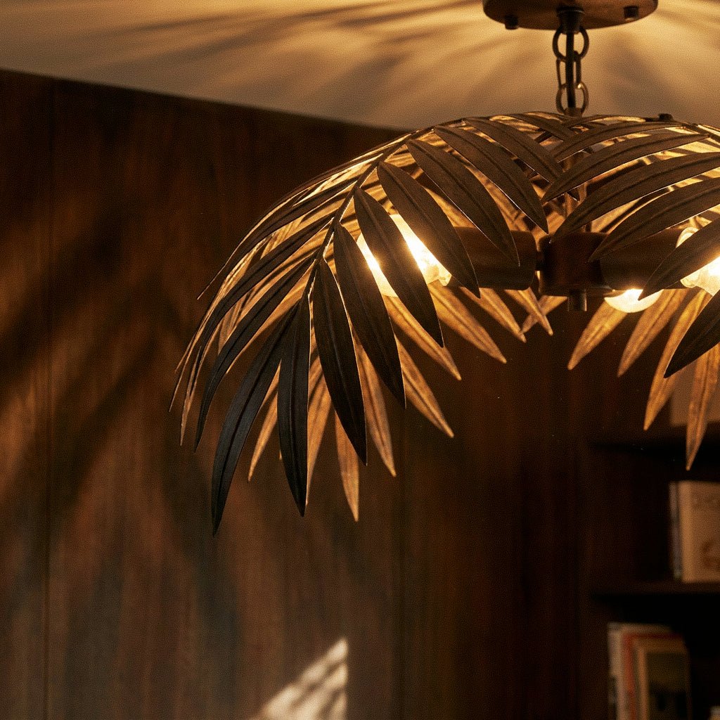 Clérachic close view of ceiling-mounted bronze palm fronds curving over glowing bulbs beside walnut panelling.