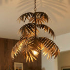 Clérachic tiered antique-gold palm-leaf chandelier close up, each iron frond catching the glow of the bulb below.