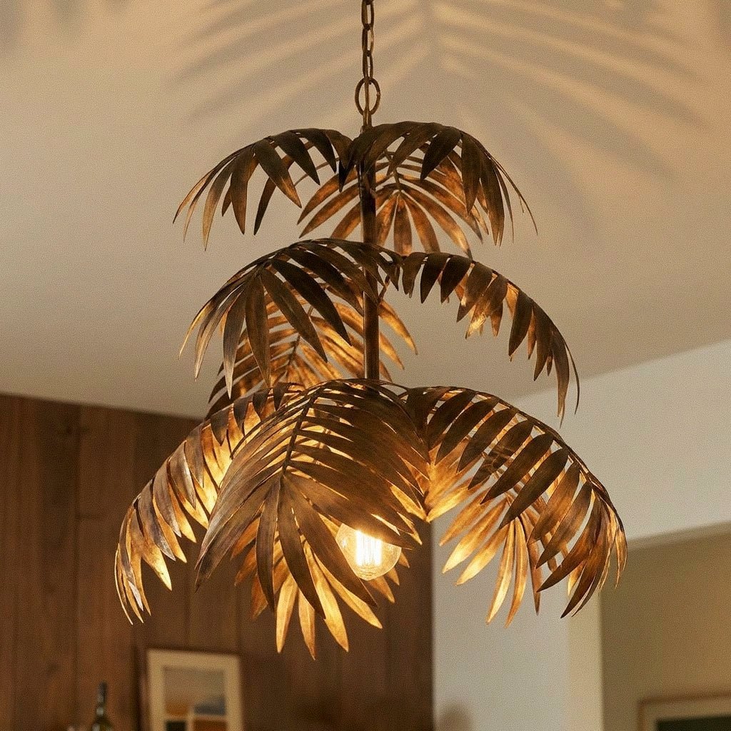 Clérachic tiered antique-gold palm-leaf chandelier close up, each iron frond catching the glow of the bulb below.