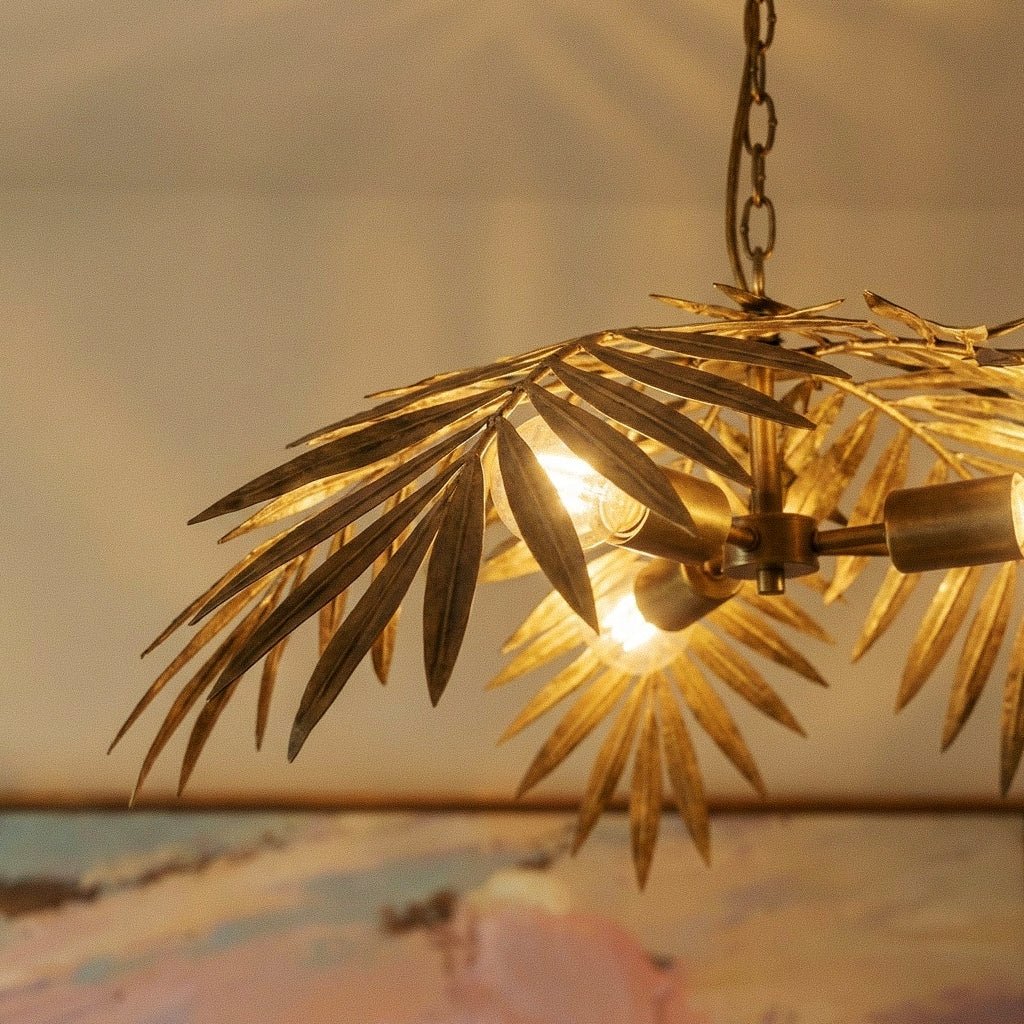 Clérachic close view of a hanging palm-leaf chandelier, antique gold iron fronds fanned around warm bulbs on a chain.