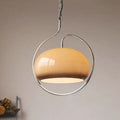 Clérachic tan glass dome pendant on a chrome hoop, hanging against a pale wall with a warm downward glow.