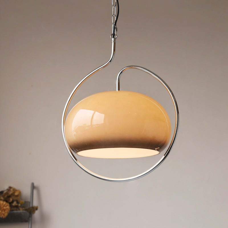 Clérachic tan glass dome pendant on a chrome hoop, hanging against a pale wall with a warm downward glow.