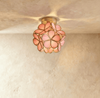 Clérachic flower ceiling light in pink glass petals on a brass mount, lit warm against a plaster ceiling.