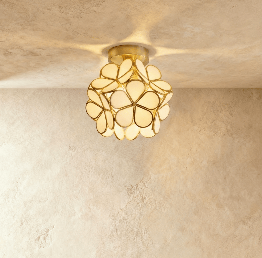 Clérachic flower ceiling light in cream glass petals on a brass mount, glowing warm on a plaster ceiling.