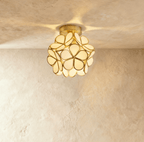 Clérachic flower ceiling light in cream glass petals on a brass mount, glowing warm on a plaster ceiling.