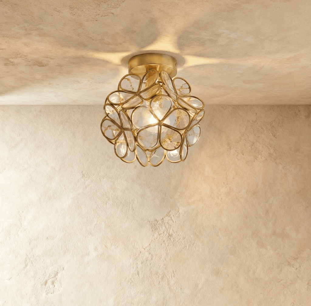 Clérachic flower ceiling light in pale glass petals flecked with tiny bubbles, lit warm on a brass mount.