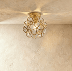 Clérachic flower ceiling light in pale glass petals flecked with tiny bubbles, lit warm on a brass mount.