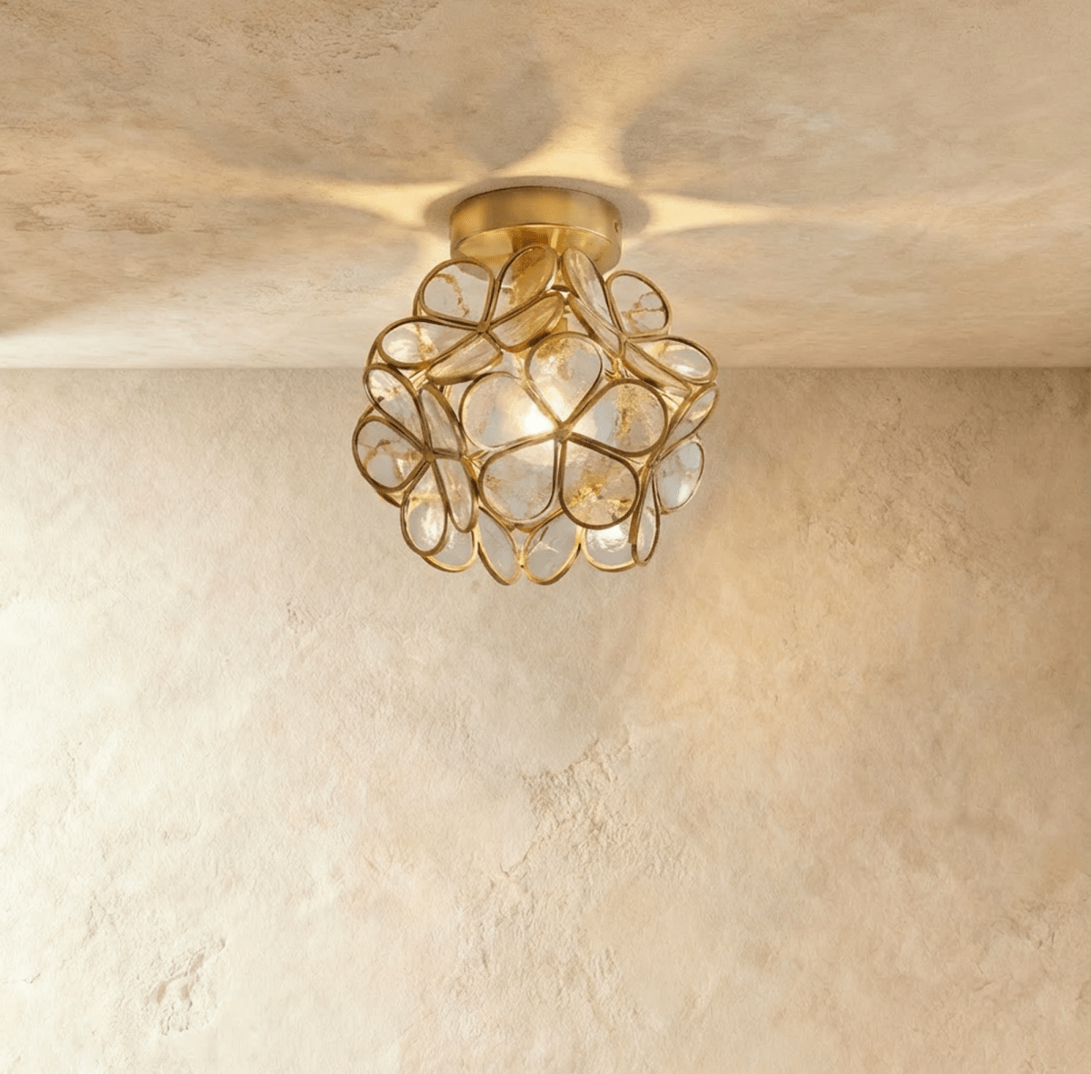 Clérachic flower ceiling light in pale glass petals flecked with tiny bubbles, lit warm on a brass mount.