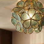 Clérachic flower ceiling light detail, sage-green ribbed glass petals lit warm around the brass frame.