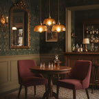 Three Clérachic brown glass pendants hung over a round wooden table with burgundy chairs, in a dark room with patterned green wallpaper.