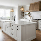 Two square-shaped Clérachic brown glass pendants in a bright kitchen, over a white island with a farmhouse sink and a wooden range hood.