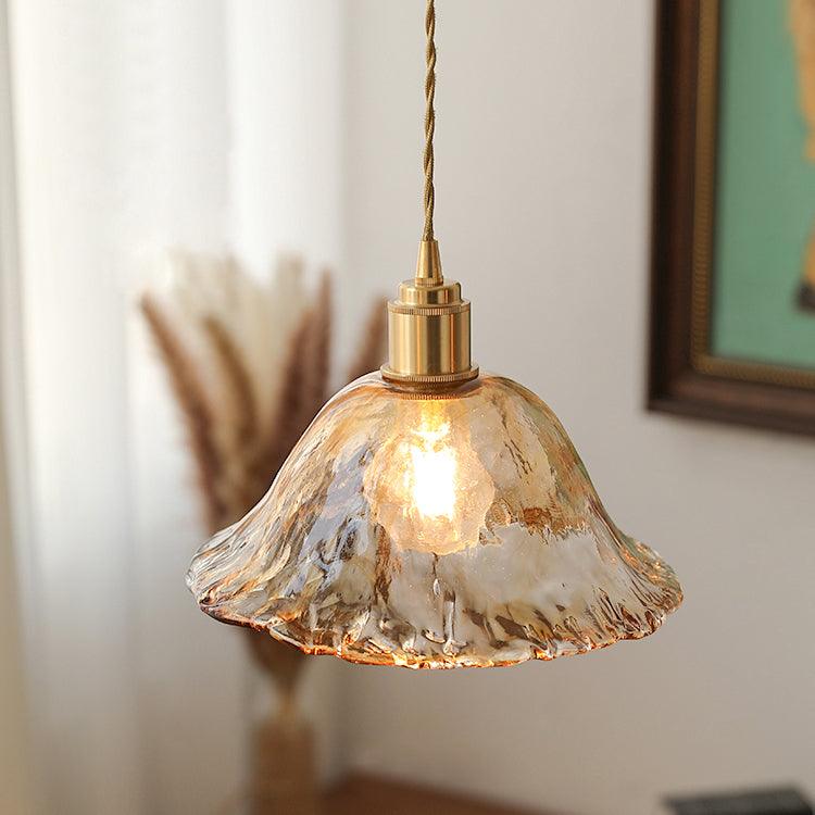 Close view of this Clérachic bell-shaped pendant in rippled amber glass, lit beside a white curtain and a stem of dried pampas grass.