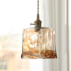 Close view of the square rippled glass shade on this Clérachic pendant, with a brass socket and switch and a soft window behind.