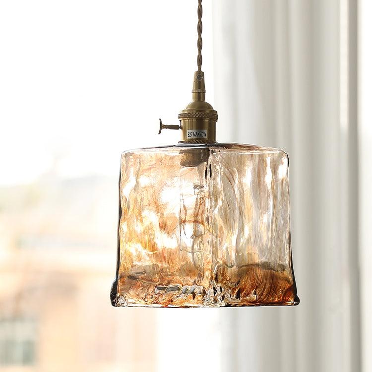 Close view of the square rippled glass shade on this Clérachic pendant, with a brass socket and switch and a soft window behind.