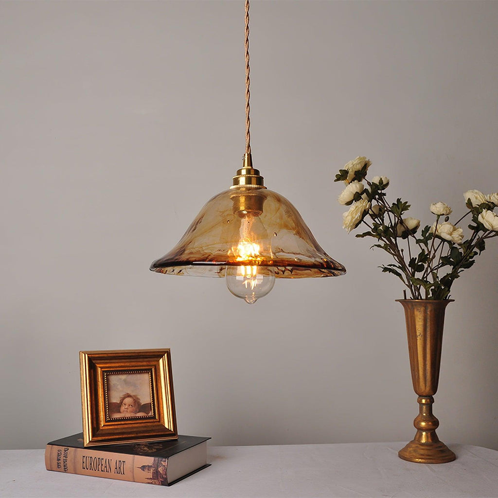 A Clérachic bell-shaped pendant in brown glass hung above a console, with a gold vase of white flowers and a framed portrait beside it.