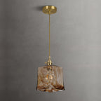 Clérachic cube pendant in swirled brown glass on a brass ceiling plate and twisted cord, hung against a grey plaster wall.