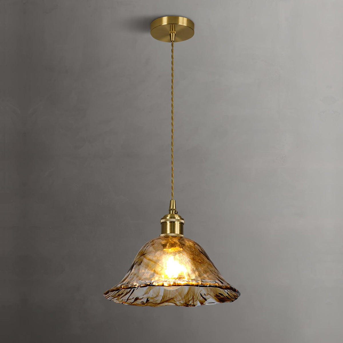 The same Clérachic bell pendant lit on a grey wall, the bulb glowing through rippled brown glass with a frilled rim.