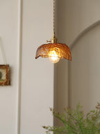 Clérachic hammered-glass dome pendant lit beside an arched white wall, with a few fern fronds in the foreground.