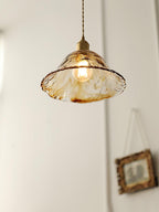Clérachic bell pendant in brown glass with a frilled rim, lit against a white wall beside a hanging gilt picture frame.