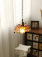 Lit Clérachic pendant with a crinkled, frilled amber glass shade, in front of sheer curtains with a bookcase and a plaster bust beside it.