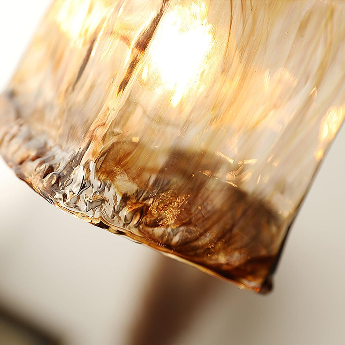 Close view of the uneven, frilled lower rim of this Clérachic brown glass shade, with dark swirls in the glass and a lit bulb.