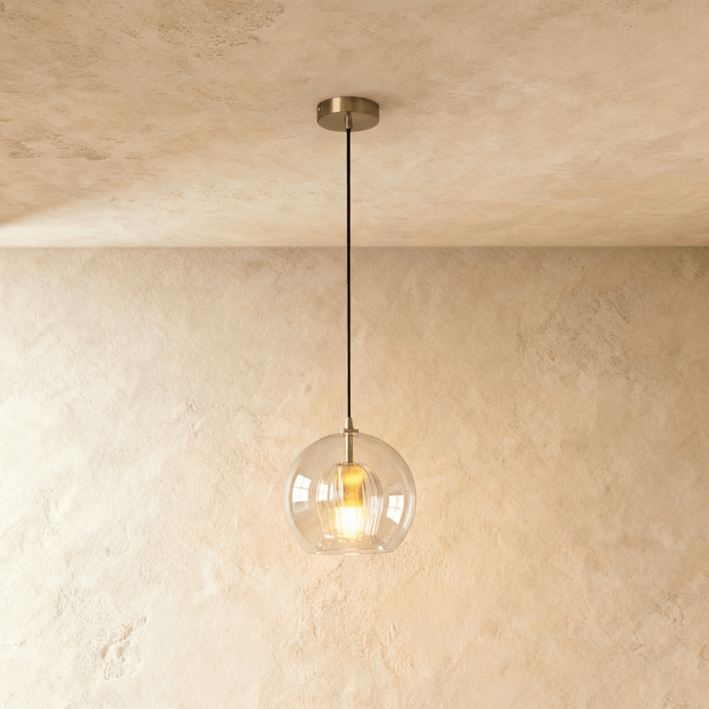 Clérachic pendant light with a clear ribbed glass globe and brass fitting, hung on a black cord from a plaster ceiling.