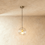 Clérachic pendant light with a clear ribbed glass globe and brass fitting, hung on a black cord from a plaster ceiling.