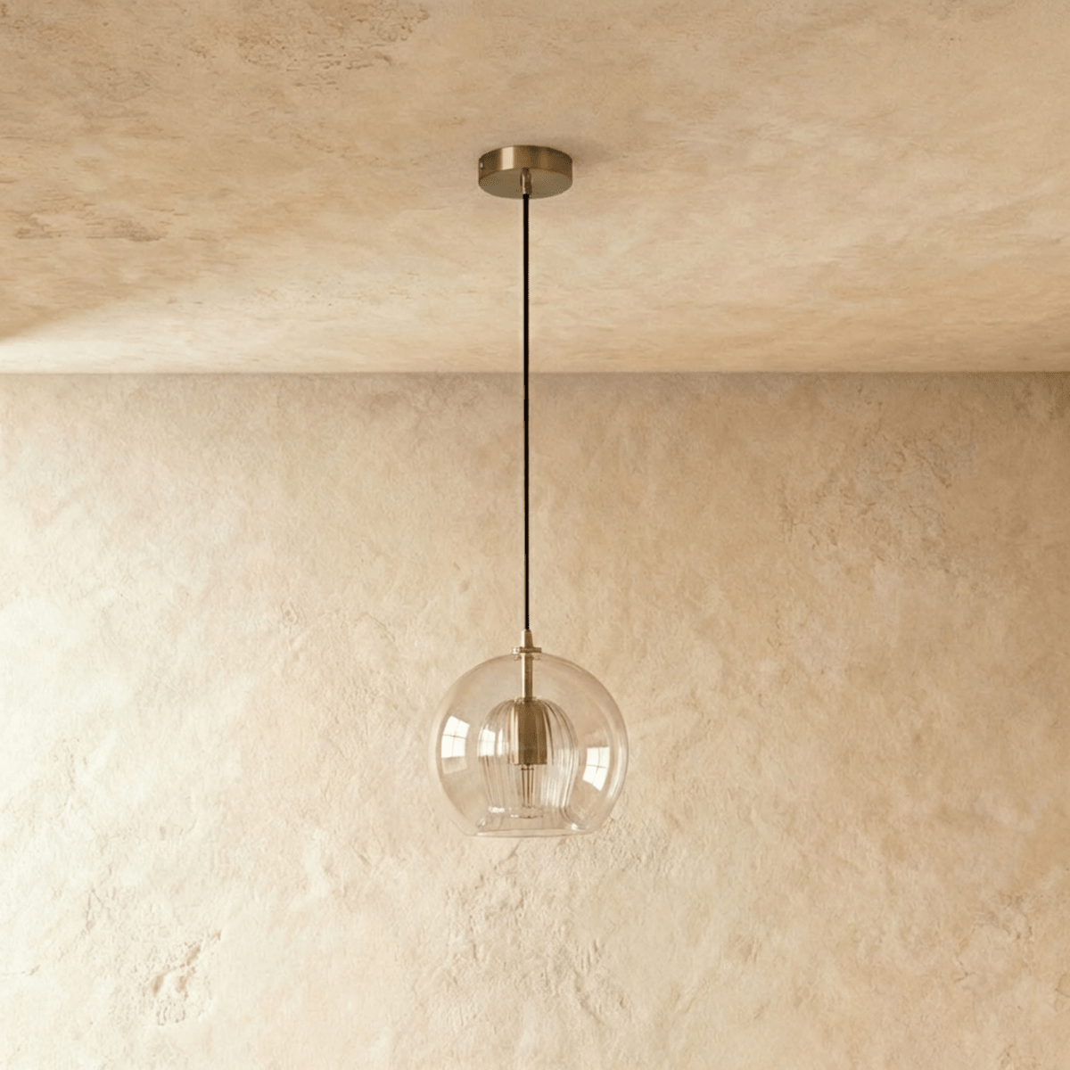 Clérachic pendant light, clear glass sphere over a fluted inner shade, brass ceiling rose against a textured wall.