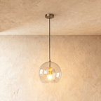 Clérachic pendant light close-up on the knurled brass ceiling rose and black cord above the glass globe shade.