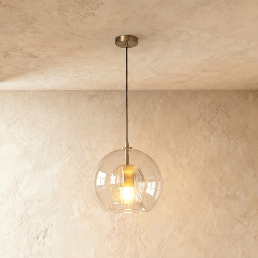 Clérachic pendant light lit warm, its clear glass globe and fluted inner shade glowing against a plaster wall.
