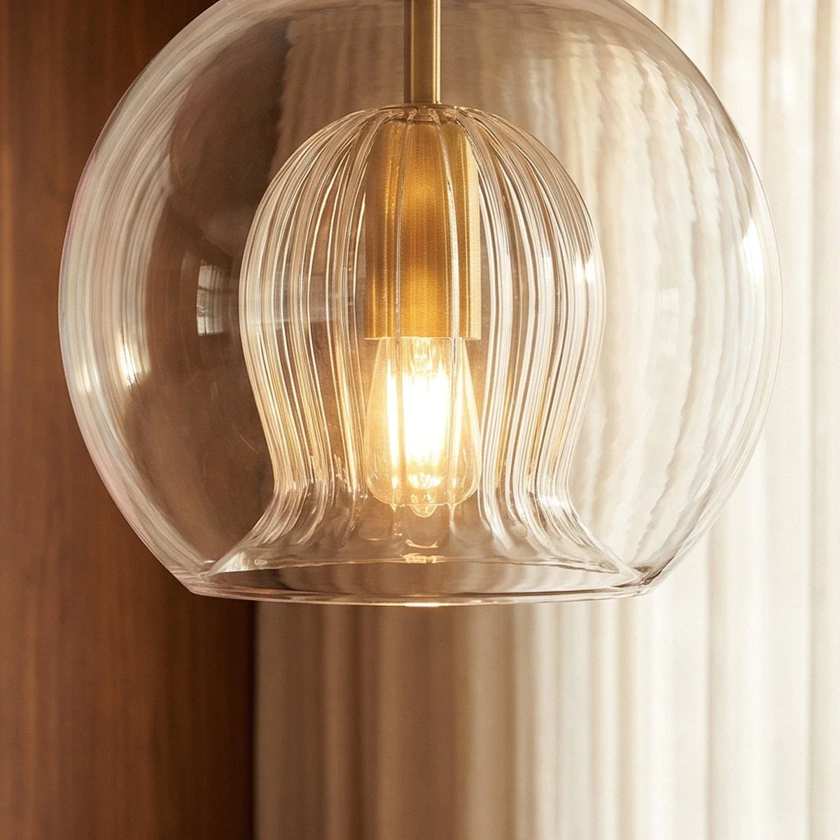 Clérachic pendant light detail, the fluted glass inner shade and brass socket glowing inside the clear outer globe.