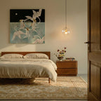 Clérachic pendant light lit warm beside a bed, its clear glass globe hanging on a slim cord in a calm bedroom.