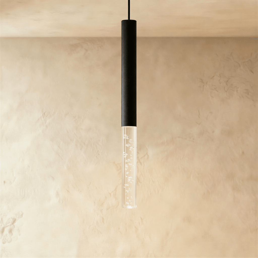 Clérachic pendant with a black cylindrical body and a longer bubble acrylic shade, glowing softly on a limewash wall.