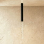Clérachic black cylinder pendant light with an extended clear acrylic shade full of tiny bubbles, shown on a plaster wall.
