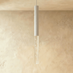 Clérachic white tube pendant light with a longer bubble acrylic shade, lit warmly against a limewash wall.
