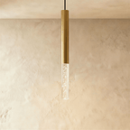Clérachic pendant light with a brushed gold aluminium tube and a short clear bubble acrylic shade, on a limewash wall.