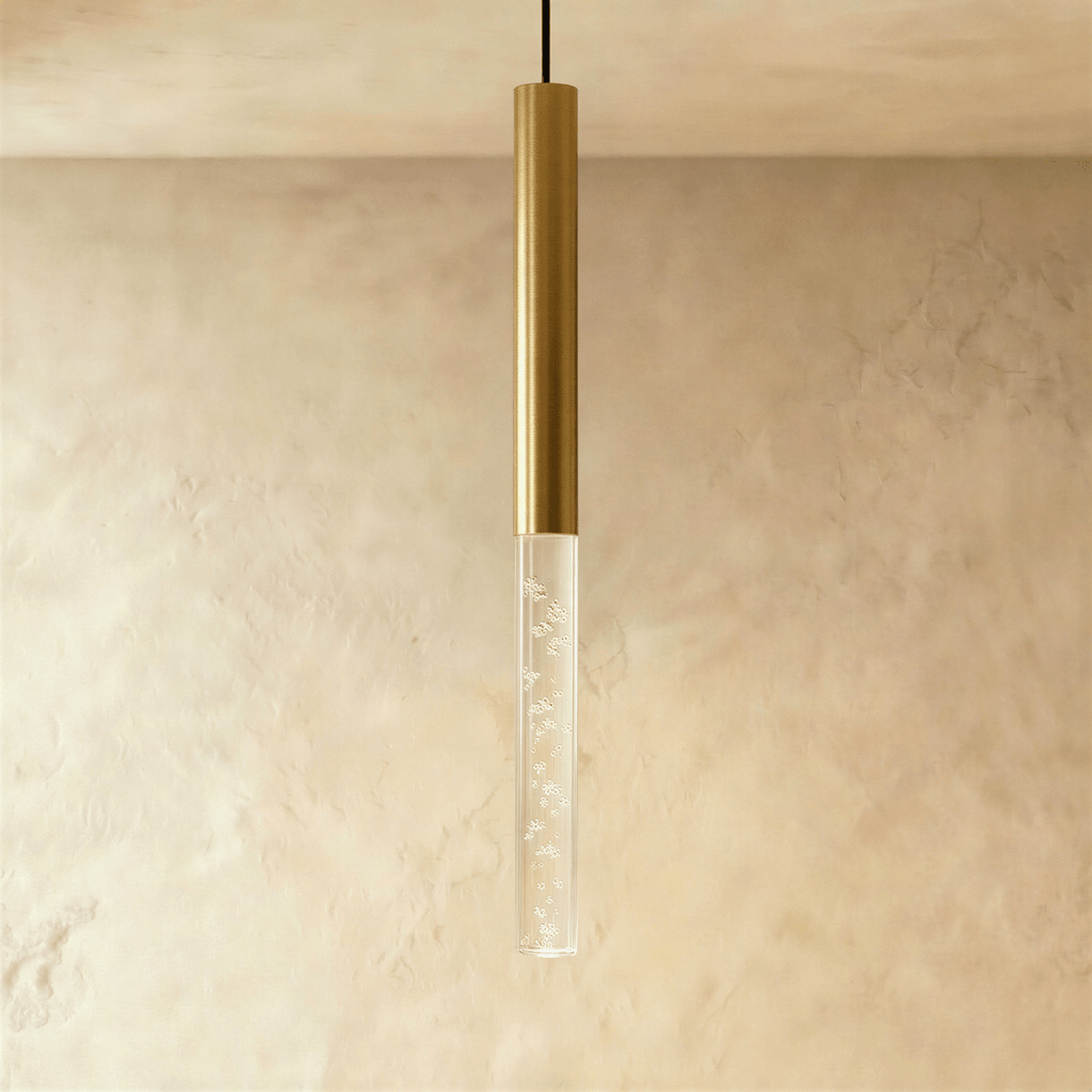 Clérachic brushed gold pendant light with a tall bubble acrylic shade, hanging against a textured limewash wall.