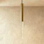 Clérachic brushed gold pendant light with a tall bubble acrylic shade, hanging against a textured limewash wall.