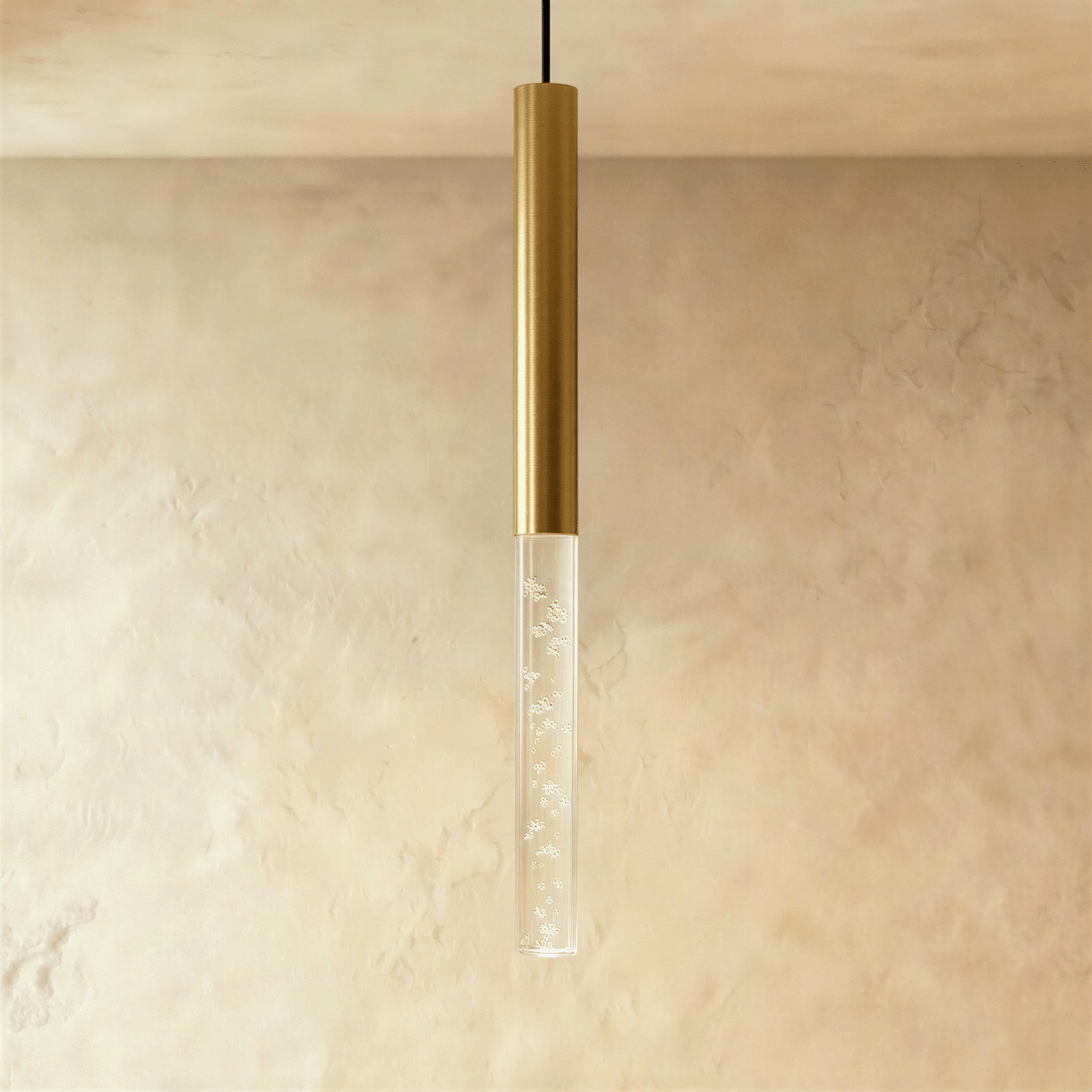 Clérachic brushed gold pendant light with a tall bubble acrylic shade, hanging against a textured limewash wall.